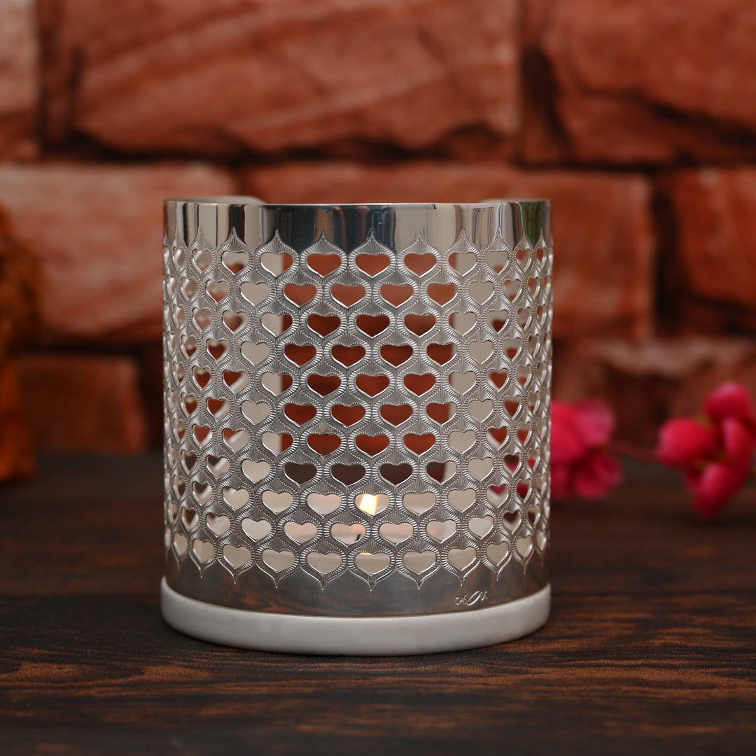 Heart Votive is a cylindrical silver candle stand pierced all over with a dense heart lattice, so a lit tealight throws a soft – Large