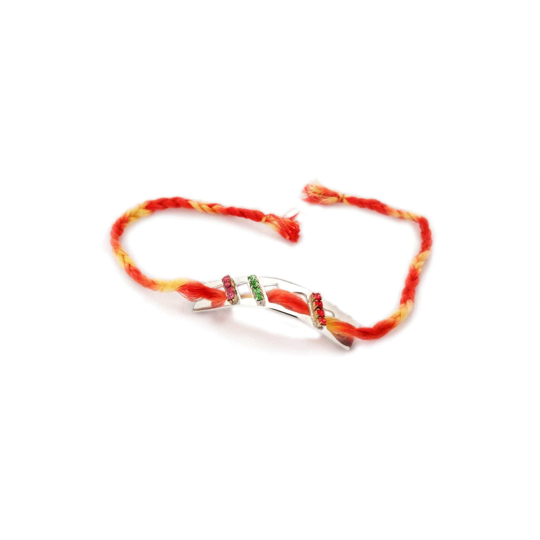 Rakhi Mauli is a silver rakhi with a curved bar set with rows of pink, green and red stones on a red and yellow braided thread. - white background