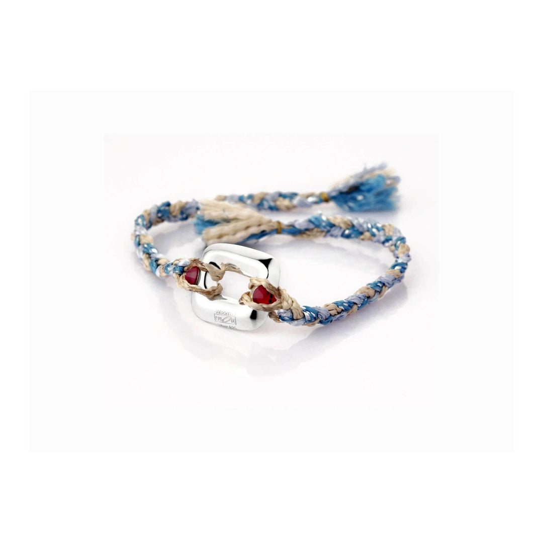 Rakhi Petite is a silver rakhi with a small rounded-square silver link set with two red stones on a blue and beige braided thread. - white background