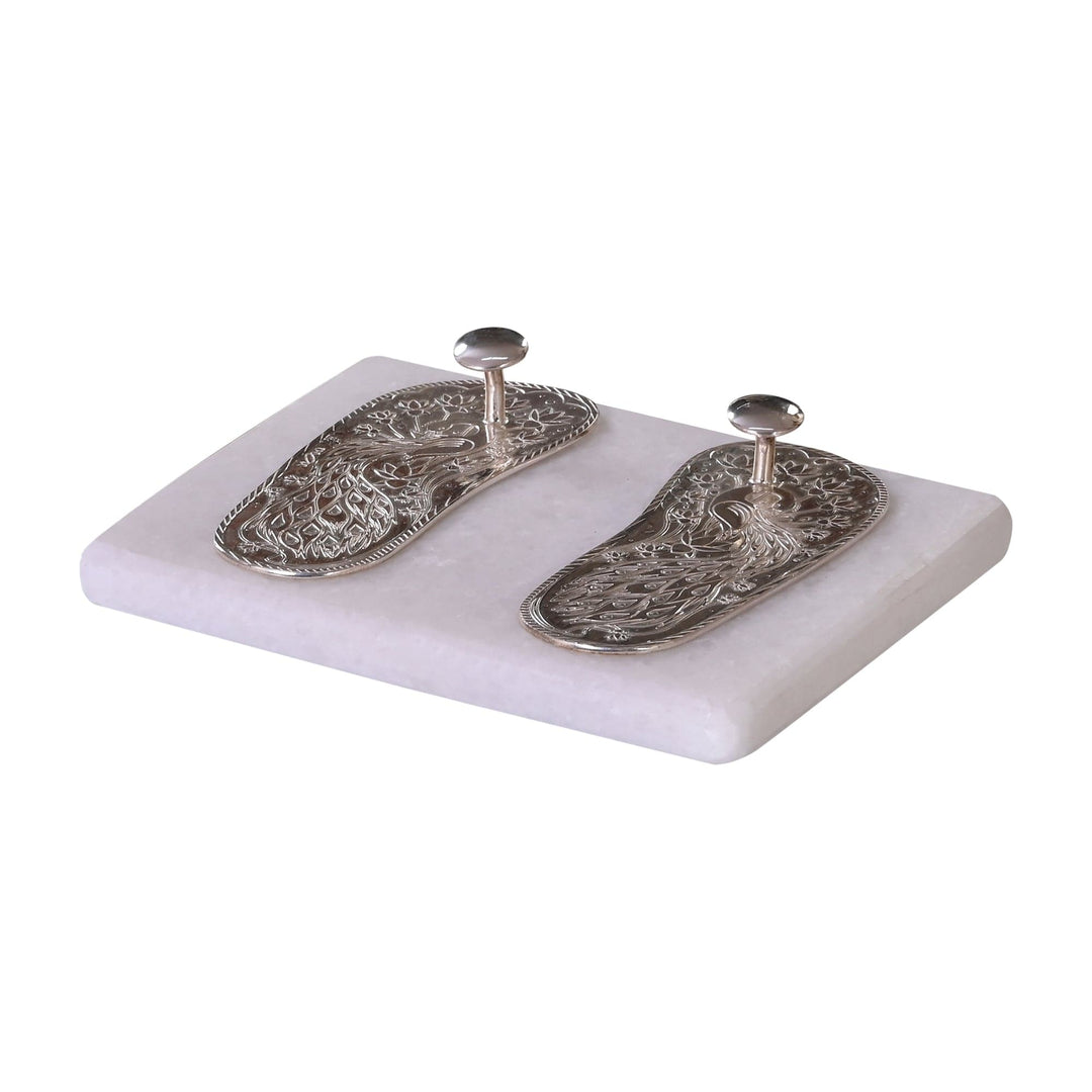 Charan Paduka is a pair of silver paduka, each engraved with a peacock and lotus motif and fitted with its own small knob - white background