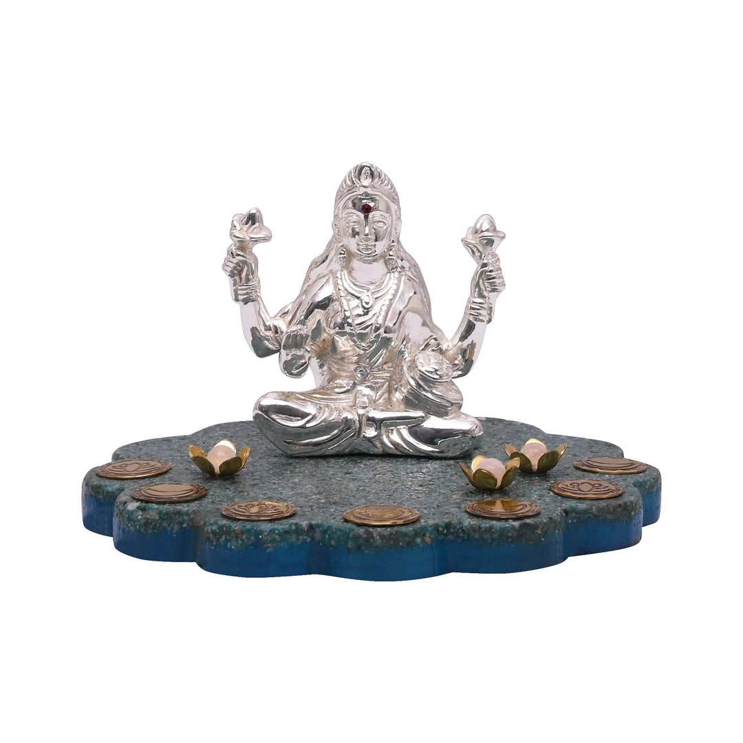 Dhana Laxmi sits a four-armed sterling silver Lakshmi idol cross-legged on a turquoise stone lotus base scattered with miniature coins and lotus diyas - white background