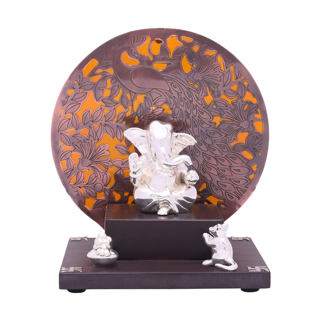 Mangalmurti Ganesha sets a sterling silver Ganesha idol before a large round copper-toned medallion cut with a peacock and floral pattern - white background