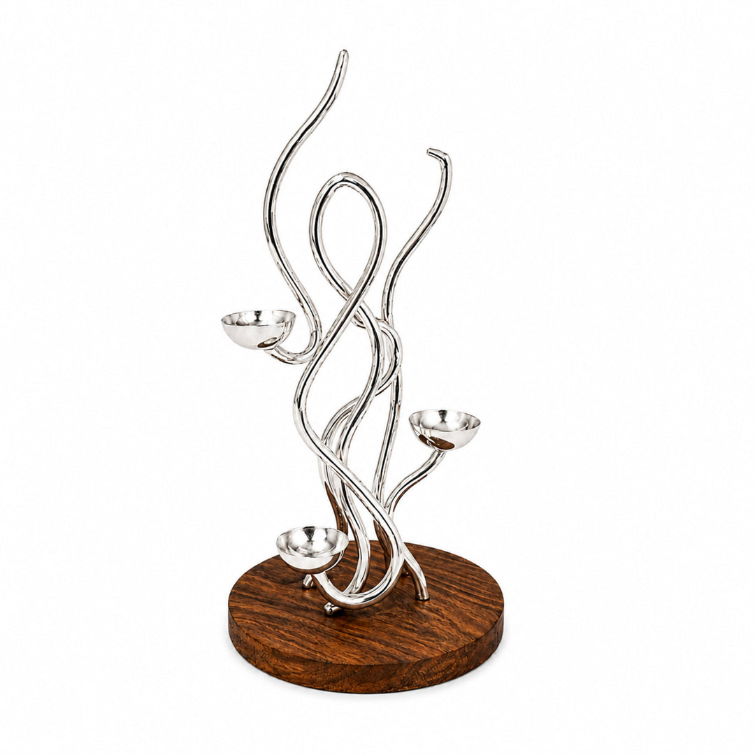 Lehar Floor Tealight Centerpiece is a silver tealight holder of interlaced polished rods rising from a dark wood plinth, with three shallow cups staggered up its height - white background