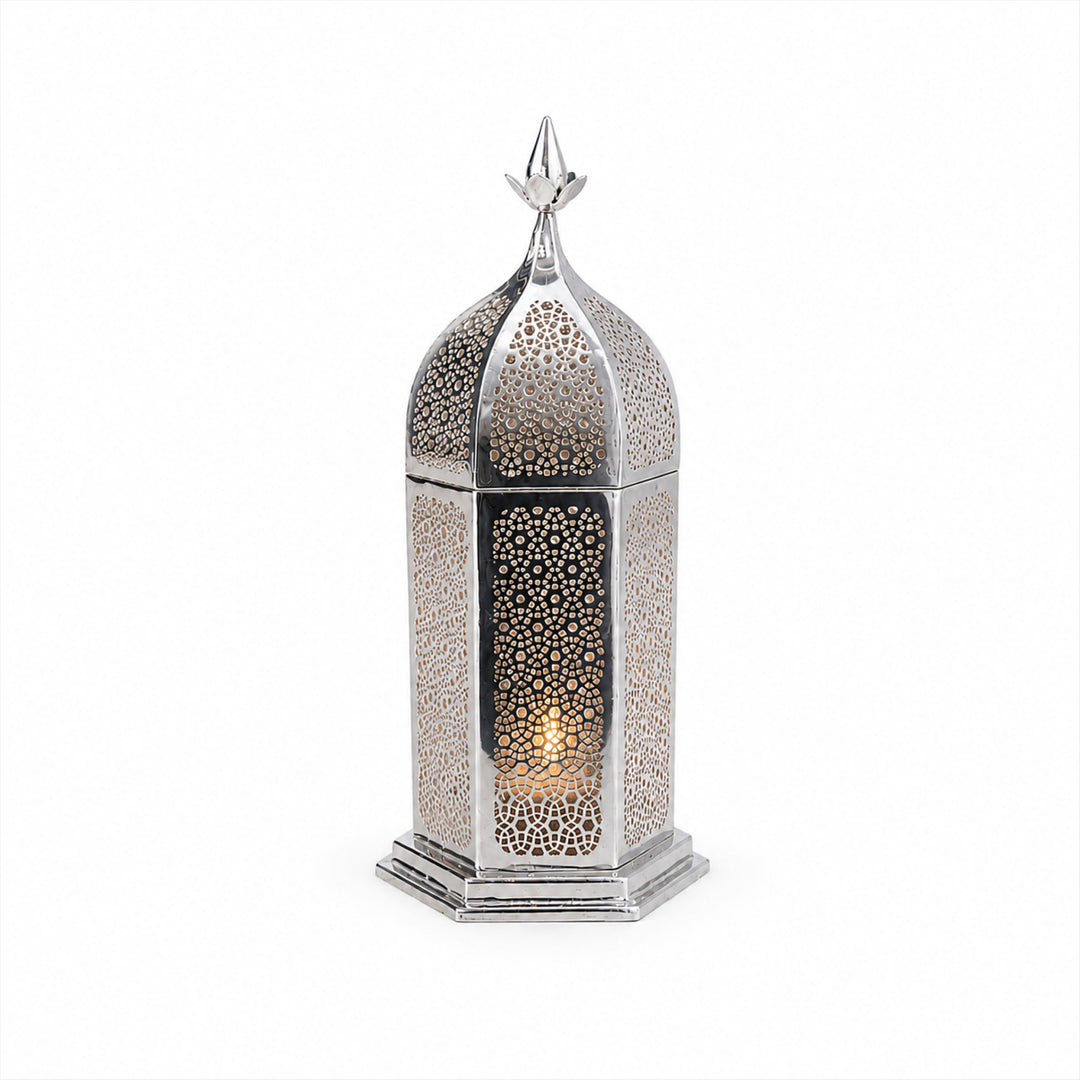 Noor Votive And Oil Burner is a silver oil burner shaped as a tall hexagonal lantern with a lace-pierced body, a lift-off ogee dome and a glass bowl seated in the neck - white background