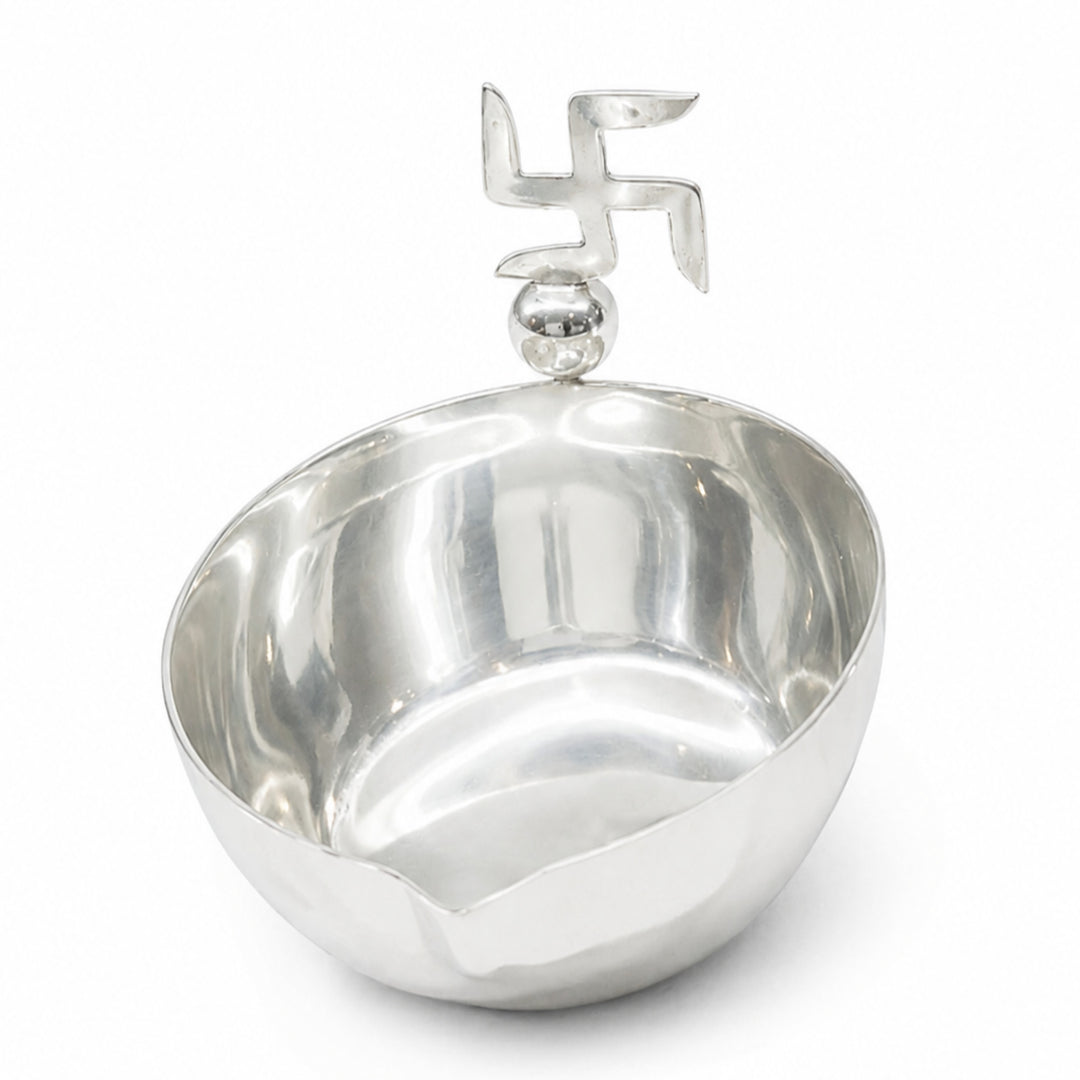 Swastik Diya is a silver diya with a plain mirrored oil bowl and a flat cut swastik standing above its waved rim - white background
