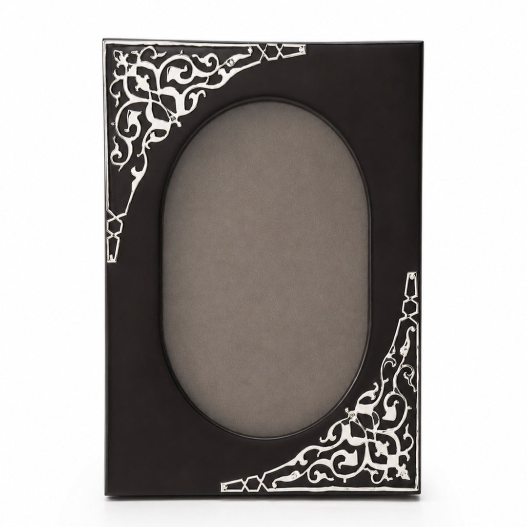 Taar Photo Frame Oval Cut is a silver photo frame with an oval aperture in a dark brown wood board and scrollwork silver corners set on one diagonal - white background