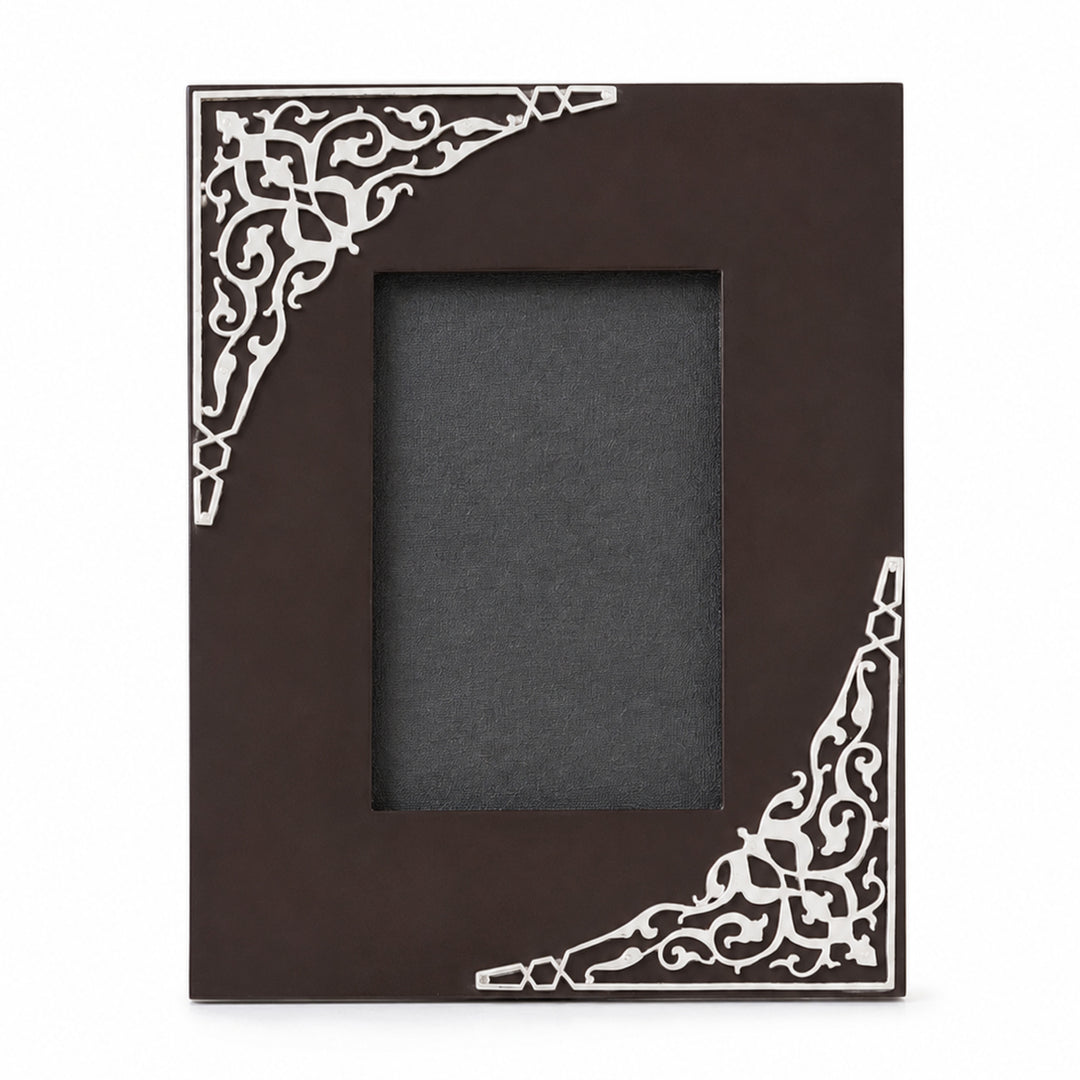Taar Photo Frame Rectangle Cut is a silver photo frame with an off-centre rectangular aperture in a dark brown wood board and scaled-up scrollwork silver corners - white background