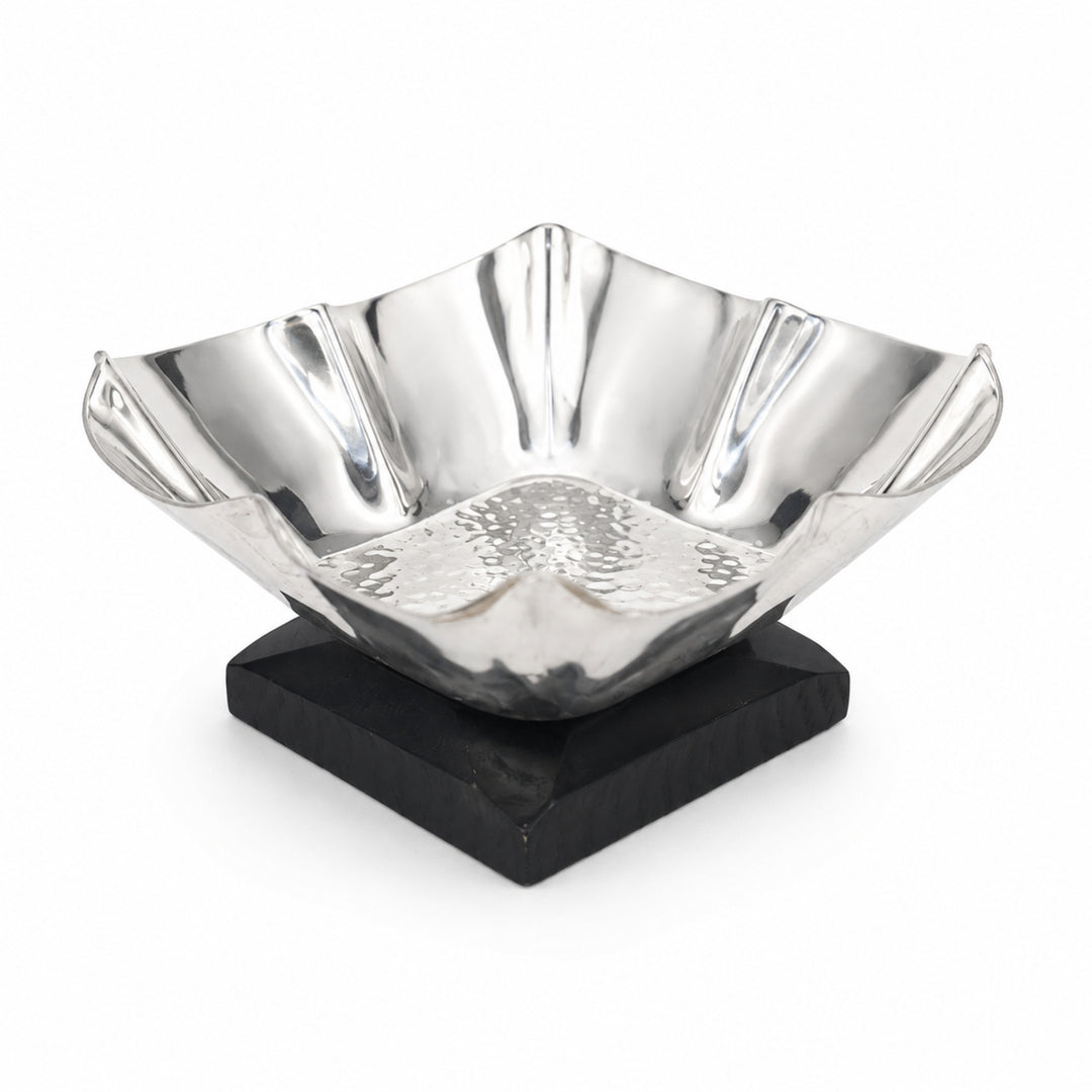 Veyra Nut Bowl is a silver nut bowl with deeply fluted walls, a petal-like waved rim and a hammered well floor, set on a black stained wood base - white background