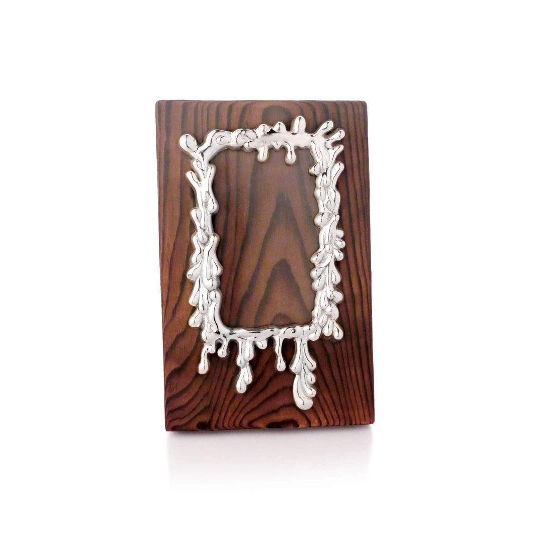 Photo Frame Melt is a sterling silver frame with a drip-like melting edge set against a dark, burnt-finish teak wood backing panel – Small