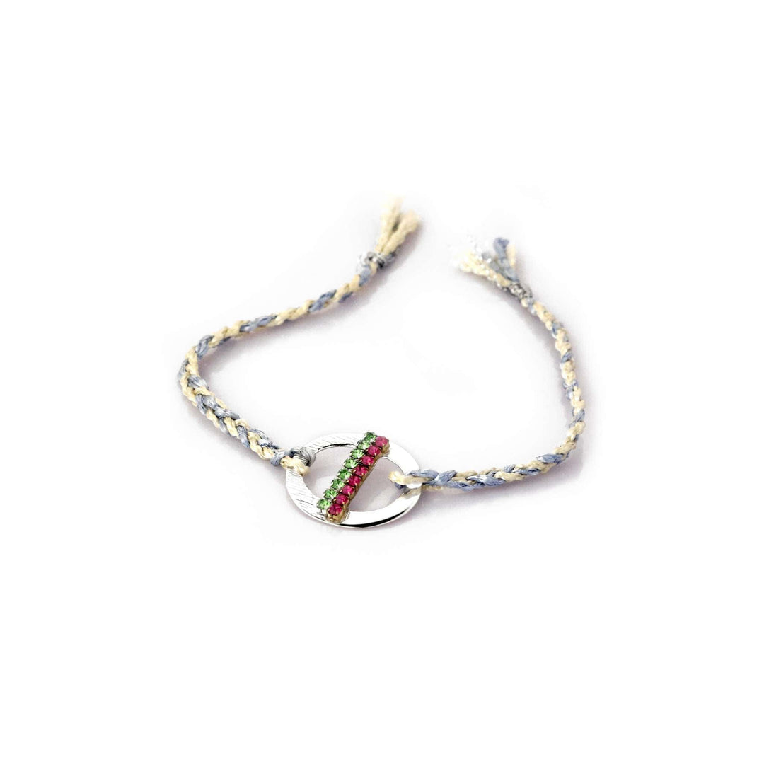 Rakhi Chroma is a silver rakhi with a round medallion set with a diagonal row of green and coral stones on a braided cream and grey-blue thread. - white background