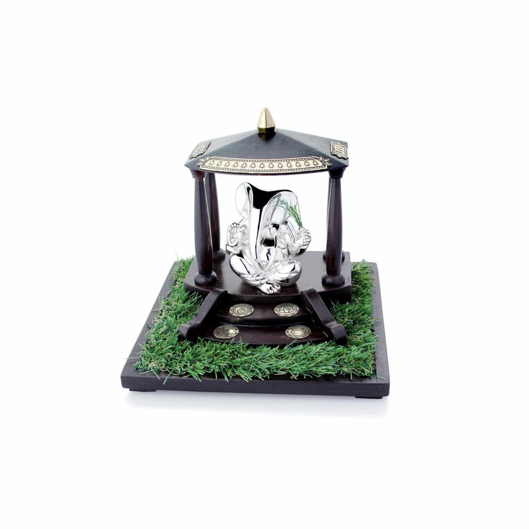 Ganesh Durva seats a sterling silver Ganesha idol cross-legged inside a miniature wood pavilion, holding a sprig of durva grass - white background
